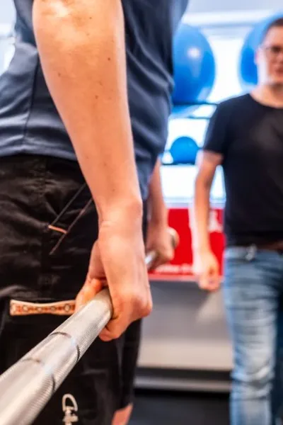 Trainer begleitet einen Klienten beim Krafttraining mit der Langhantel im Fitnessraum.