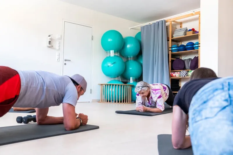 Teilnehmer trainieren gemeinsam in Unterarmstütz-Position während eines Kurses im Therapiezentrum.